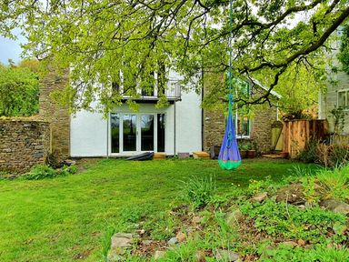 A garden with grass plants and a hanging swing in front of a house with stone and white walls at Cringoed House in Llanarth near Aberaeron