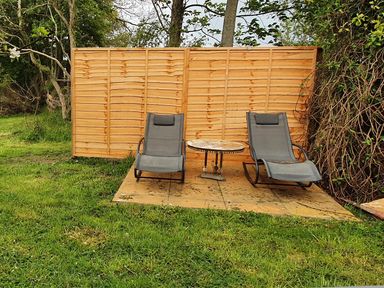 Two reclining chairs and a small round table on a paved area in a garden with a wooden fence behind at Cringoed House in Llanarth near Aberaeron