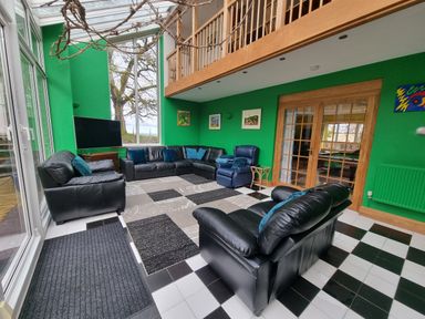 A lounge area with black leather sofas a blue armchair a patterned rug and green walls at Cringoed House in Llanarth near Aberaeron