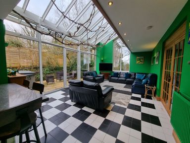 A sunroom with black leather sofas a patterned rug black and white tiled floor green walls and large glass windows at Cringoed House Llanarth near Aberaeron