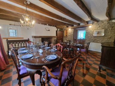 A dining room with two wooden tables set with plates and glasses and wooden chairs with purple cushions at Cringoed House Llanarth near Aberaeron
