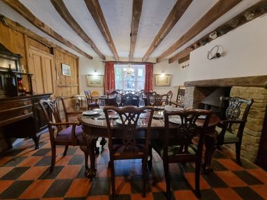 A dining room with a wooden table and chairs set on a checkered floor with wooden beams on the ceiling at Cringoed House Llanarth near Aberaeron