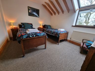 A bedroom with two single beds bedside tables and lamps a window and an armchair at Cringoed House Llanarth near Aberaeron