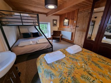 A bedroom with bunk beds armchair wardrobe and a bed with tropical patterned bedspread at Cringoed House Llanarth near Aberaeron