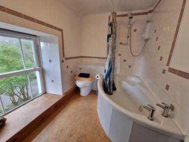 A bathroom with a large window a toilet with folded towels a bathtub with a shower curtain and a shower unit at Cringoed House Llanarth near Aberaeron