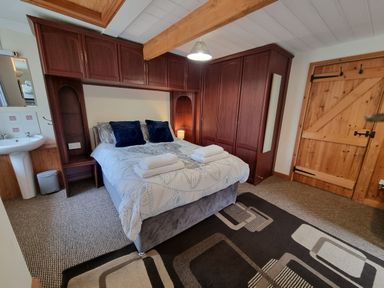 A bedroom with a bed with towels pillows wooden wardrobes a wooden door a sink and a rug on the floor at Cringoed House Llanarth near Aberaeron