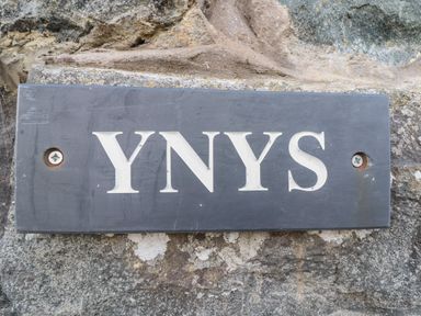 A black rectangular sign with the text YNYS mounted on a stone wall at Ynys in Dyffryn Ardudwy