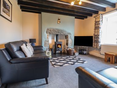 A living room with a black leather sofa a wood burning stove and a television at Ynys in Dyffryn Ardudwy