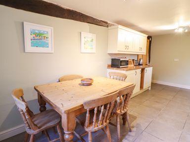 A kitchen with a wooden dining table and chairs white cabinets and appliances at Ynys in Dyffryn Ardudwy