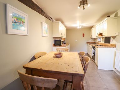 A kitchen with a wooden dining table and chairs and white cabinets at Ynys in Dyffryn Ardudwy