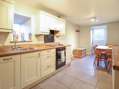 A kitchen with cream cabinets wooden countertops a stove a dining table with chairs and a door at Ynys in Dyffryn Ardudwy
