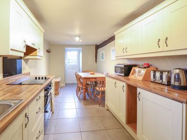 A kitchen with wooden countertops cabinets a dining table chairs and appliances at Ynys in Dyffryn Ardudwy