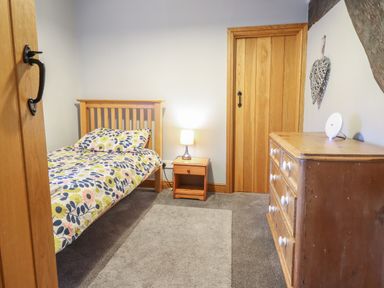 A bedroom with a single bed a nightstand with a lamp and a wooden dresser at Ynys in Dyffryn Ardudwy
