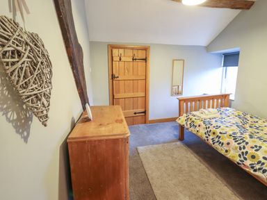 A bedroom with a wooden bed with floral bedding a wooden dresser a door a mirror and a window at Ynys in Dyffryn Ardudwy