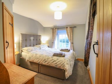 A bedroom with a double bed between two wooden doors and a window with curtains at Ynys in Dyffryn Ardudwy