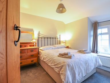 A bedroom with a double bed a wooden dresser with a mirror and lamps and a window with curtains at Ynys in Dyffryn Ardudwy