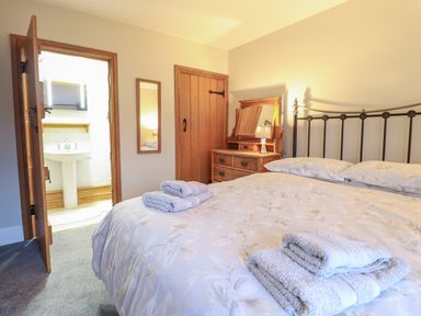 A bedroom with a bed, folded towels on the bed, a wooden dresser with a mirror and lamp, an open door leading to a bathroom at Ynys in Dyffryn Ardudwy