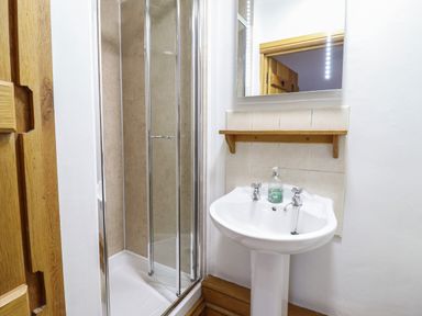 A bathroom with a glass shower enclosure a white pedestal sink and a wall mirror at Ynys in Dyffryn Ardudwy