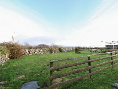 An enclosed grassy yard with wooden and stone fences and a rotary clothesline at Ynys in Dyffryn Ardudwy