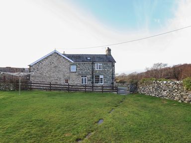 A stone house with a fenced yard and a grassy lawn with a rotary clothesline at Ynys in Dyffryn Ardudwy