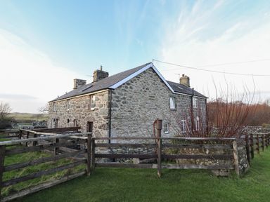 An exterior view of a stone house with a fenced yard and grassy lawn at Ynys in Dyffryn Ardudwy