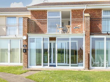 Front view of a brick two-story house with glass sliding doors on the ground floor and a balcony with table and chairs on the upper floor at Gull Cottage in Kessingland