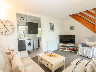 A living room with sofas coffee table television and a view into the kitchen at Gull Cottage in Kessingland