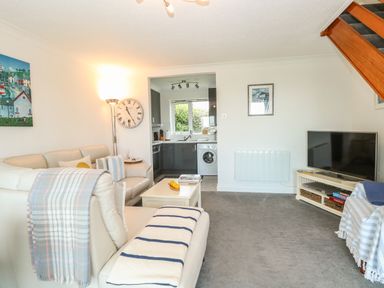 A living room with white sofas and a coffee table next to a kitchen with a washing machine at Gull Cottage in Kessingland