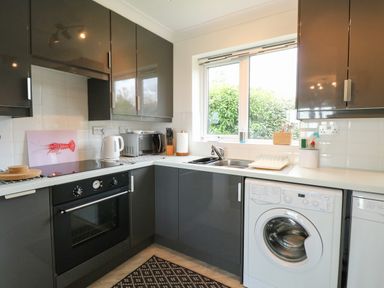 A kitchen with dark cabinets an oven microwave kettle washing machine and a window at Gull Cottage in Kessingland
