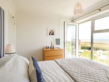 A bedroom with a bed pillow chest of drawers and an open glass door leading to a balcony at Gull Cottage in Kessingland