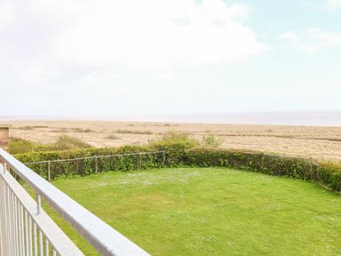 A fenced green lawn with small flowers overlooking a sandy beach and sea at Gull Cottage in Kessingland
