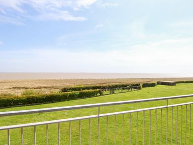 View of a grassy lawn with hedges and a railing overlooking a sandy beach and the sea at Gull Cottage in Kessingland
