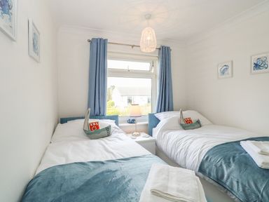 A bedroom with two single beds a lamp on a nightstand and blue curtains at Gull Cottage in Kessingland