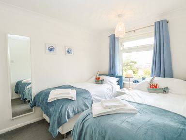 A bedroom with two beds blue blankets white towels a window with blue curtains and a mirror on the wall at Gull Cottage in Kessingland