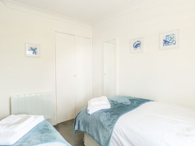 A bedroom with two single beds with blue blankets and white towels on each at Gull Cottage in Kessingland