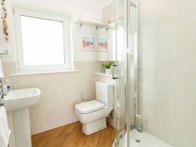 A bathroom with a toilet sink shower and a window at Gull Cottage in Kessingland