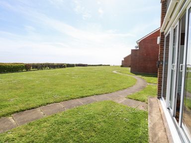 A garden area with a curved paved walkway beside brick buildings at Gull Cottage in Kessingland