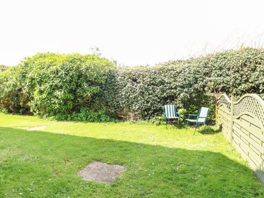 A garden with two green striped chairs on grass beside a hedge and wooden fence at Gull Cottage in Kessingland