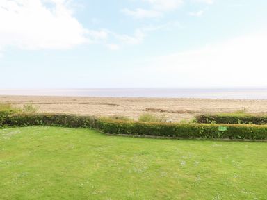 A green lawn with a hedge and a beach beyond at Gull Cottage in Kessingland