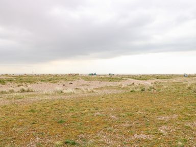 A grassy and pebbly coastal landscape with small boats in the distance at Gull Cottage in Kessingland