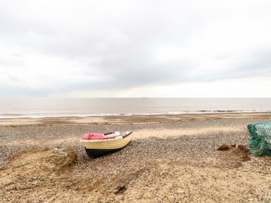 A small boat on a pebbled beach near the sea with a cloudy sky at Gull Cottage in Kessingland