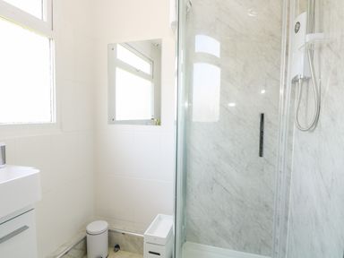 A bathroom with a shower area a trash bin a small cabinet a window and a mirror at Dollys Lookout Kessingland