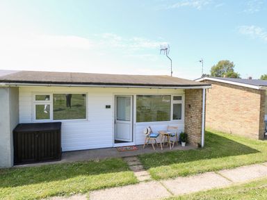 The front of a single story house with a small outdoor table and two chairs on a patio at Dollys Lookout in Kessingland