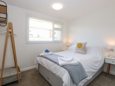A bedroom with a bed white bedding and a gray runner two bedside tables with lamps and a window with blinds at Dollys Lookout in Kessingland