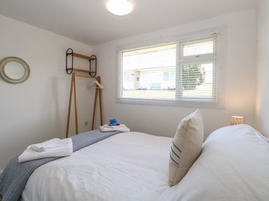A bedroom with a bed folded towels a wooden clothes rack a wall mirror and a window with blinds at Dollys Lookout in Kessingland