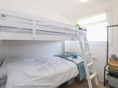 A bedroom with a white bunk bed a ladder a window and a shelving unit with baskets at Dollys Lookout in Kessingland