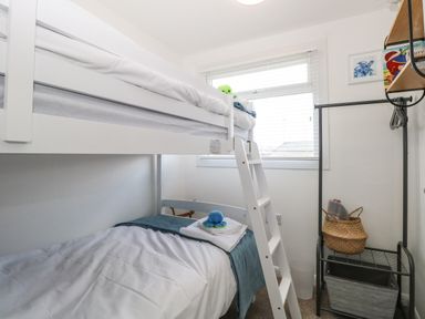A bedroom with a white bunk bed small open wardrobe and a window at Dollys Lookout in Kessingland