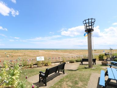 A coastal park area with benches a wooden beacon a flag and a view of the sea at Dollys Lookout in Kessingland