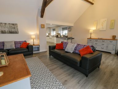 A living room with two black sofas with pillows a wooden table a sideboard and an open kitchen area at Bodrual Cottage in Rhosbodrual near Caernarfon