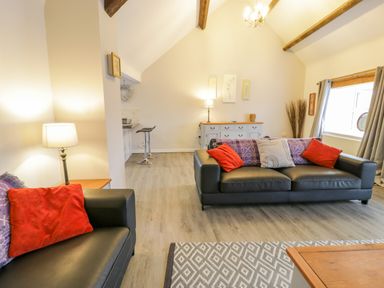 A living room with two black sofas with red and patterned cushions a wooden sideboard and bar stools at Bodrual Cottage in Rhosbodrual near Caernarfon